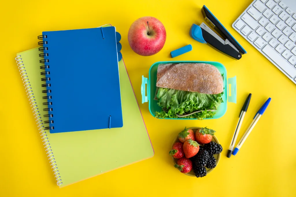 mesa com material escolar e um lanche saudável.