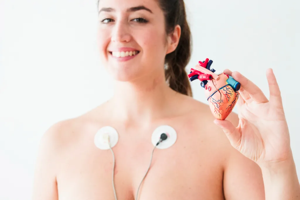 mulher com eletrodos o peito segurando uma maquete do coração.